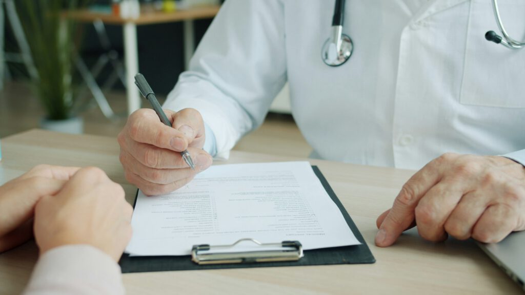 Arzt, der auf eine Patientenakte schreibt während ein Aufklärungsgespräch